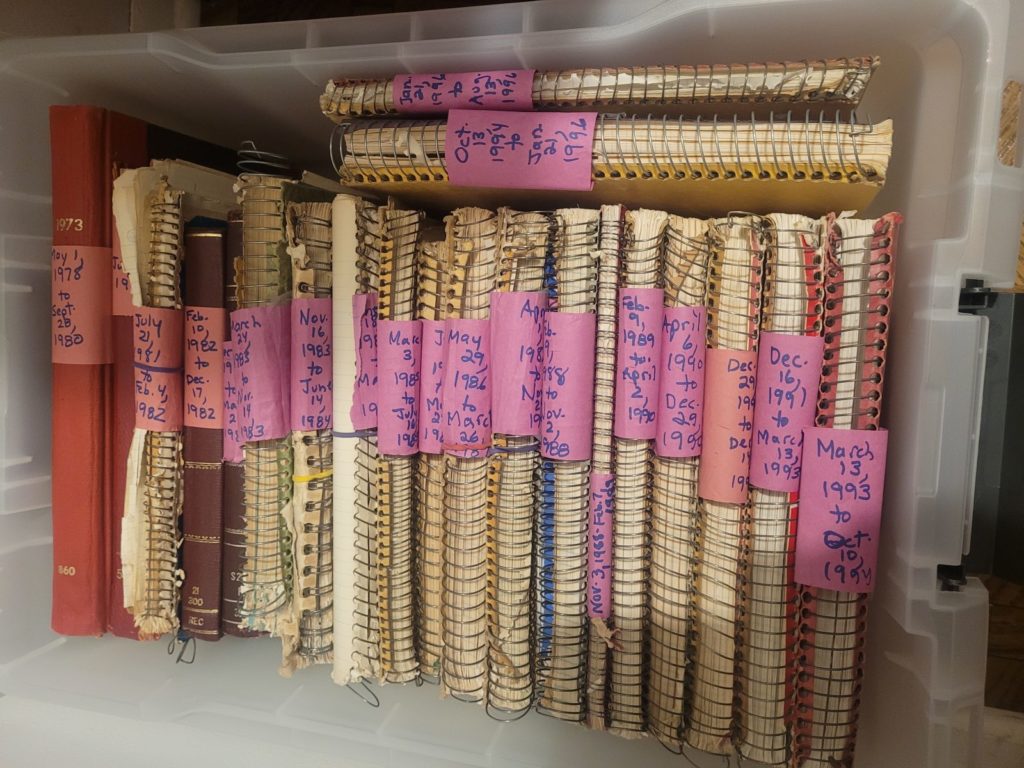 A plastic tub filled with written-in journals, most of them spiral notebooks
