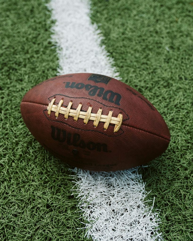 An official NFL football straddles a yard line on a football field.