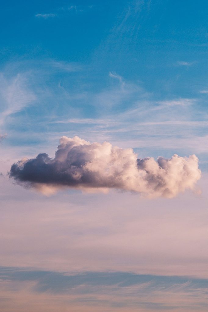 A shadowed fluffy white-grey cloud floating in a vivid blue sky with pink background clouds