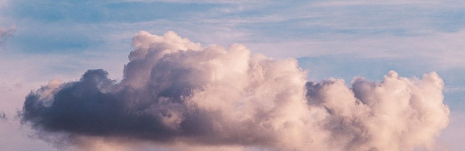 A shadowed fluffy white-grey cloud floating in a vivid blue sky with pink background clouds
